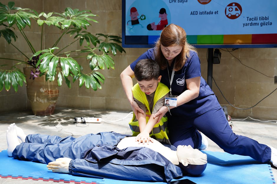 Trainer guiding a boy as they perform chest compressions on a CPR manikin on a blue mat during a training session.
