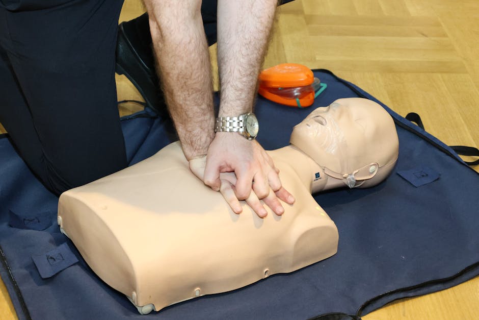 Person performing chest compressions on a CPR training dummy on a blue mat in a training setting.